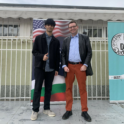 Rahil standing with another man beside the U.S. and Bulgarian flags
