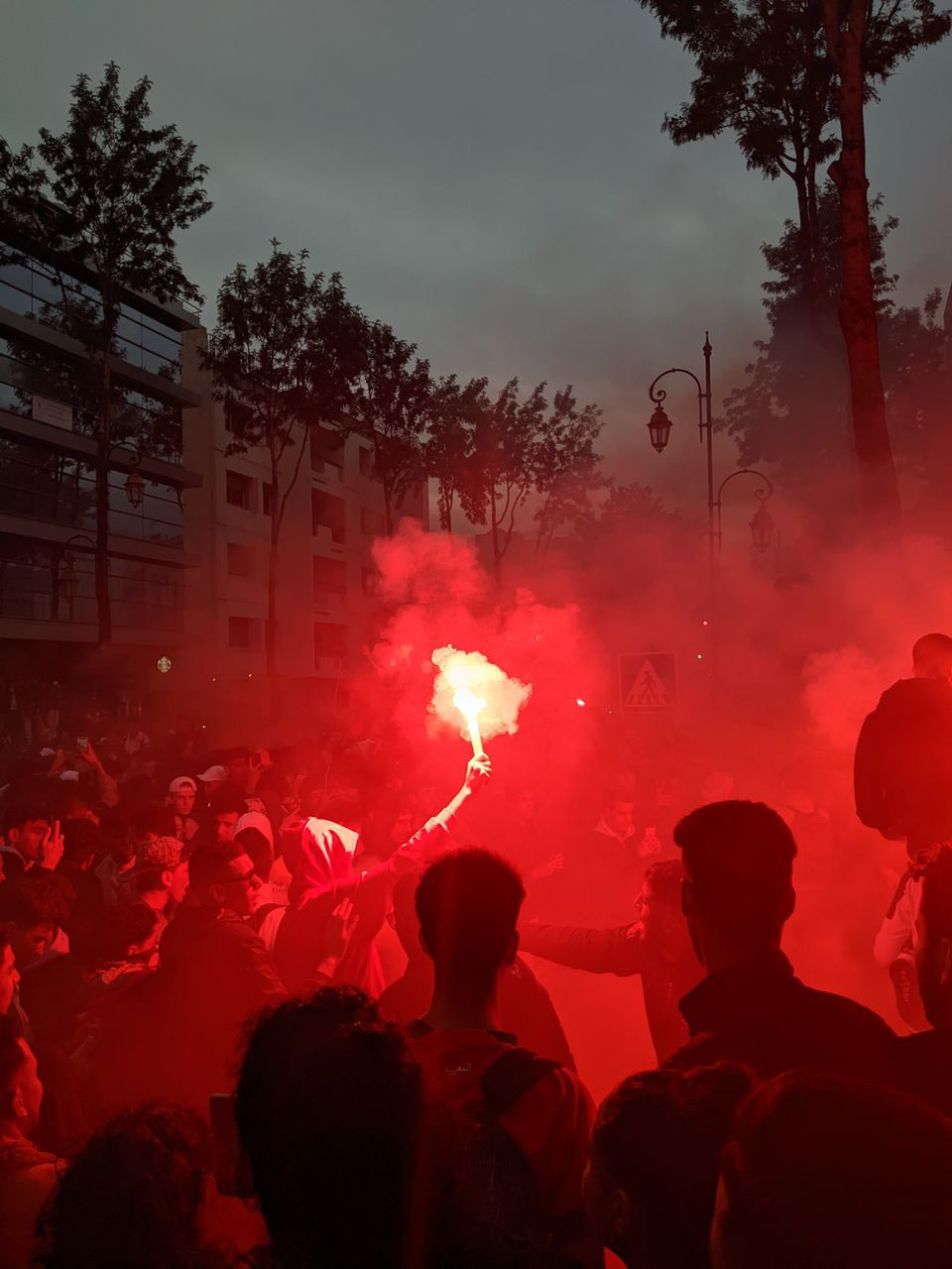 A crowd in the street at night with a red flare shooting up