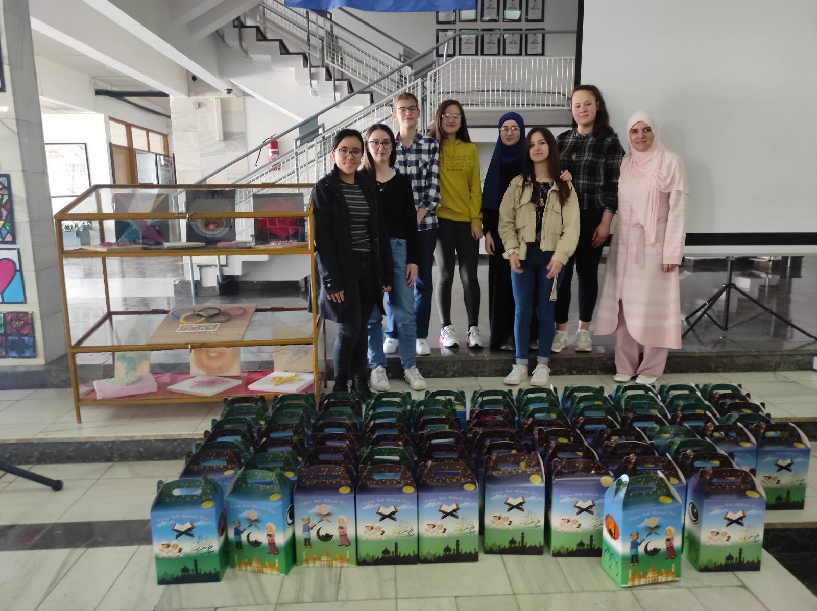 Chloe and a group of student standing in front of donation boxes for Eid.