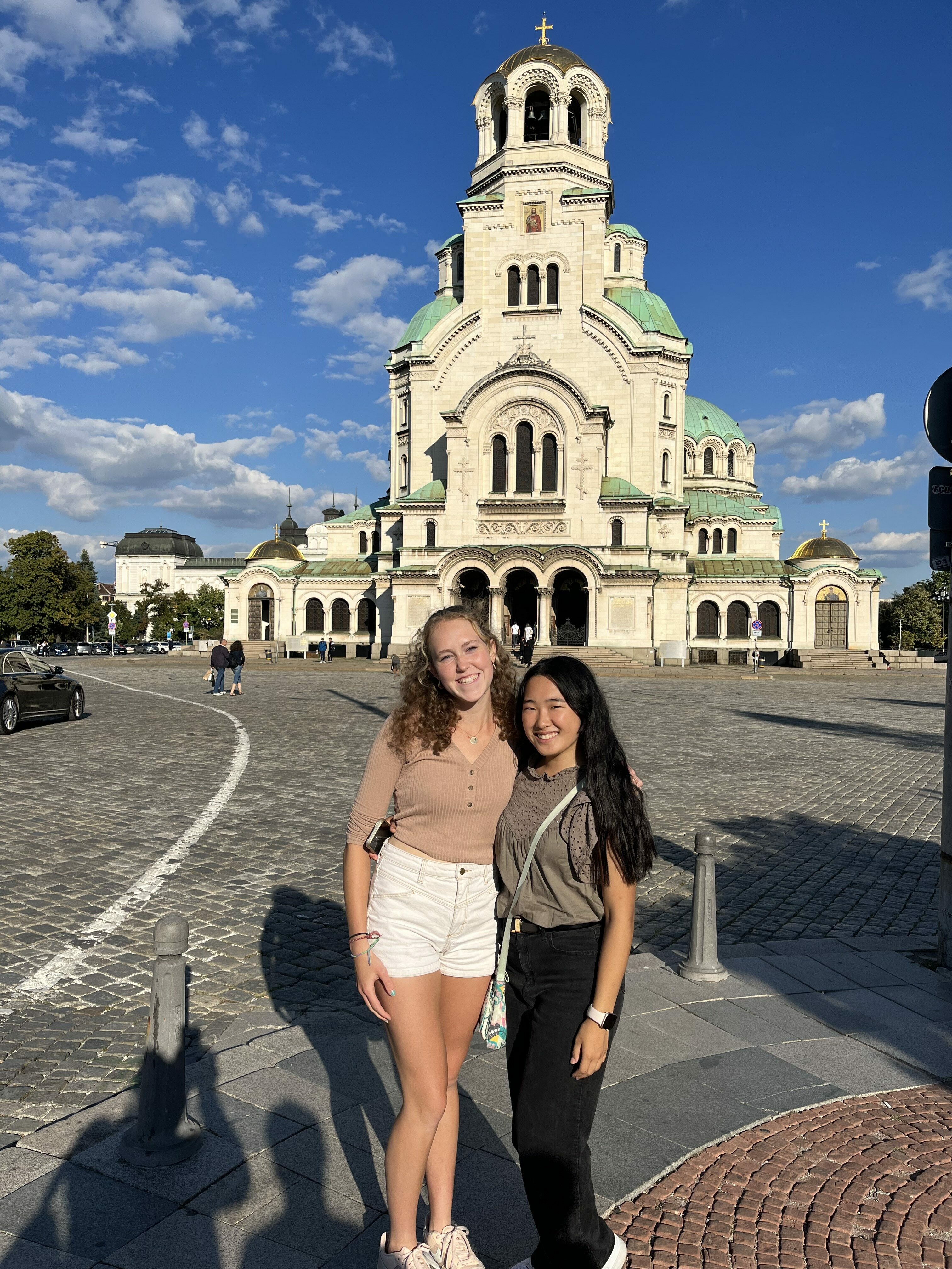 Two young women standing in front of a historical looking building 