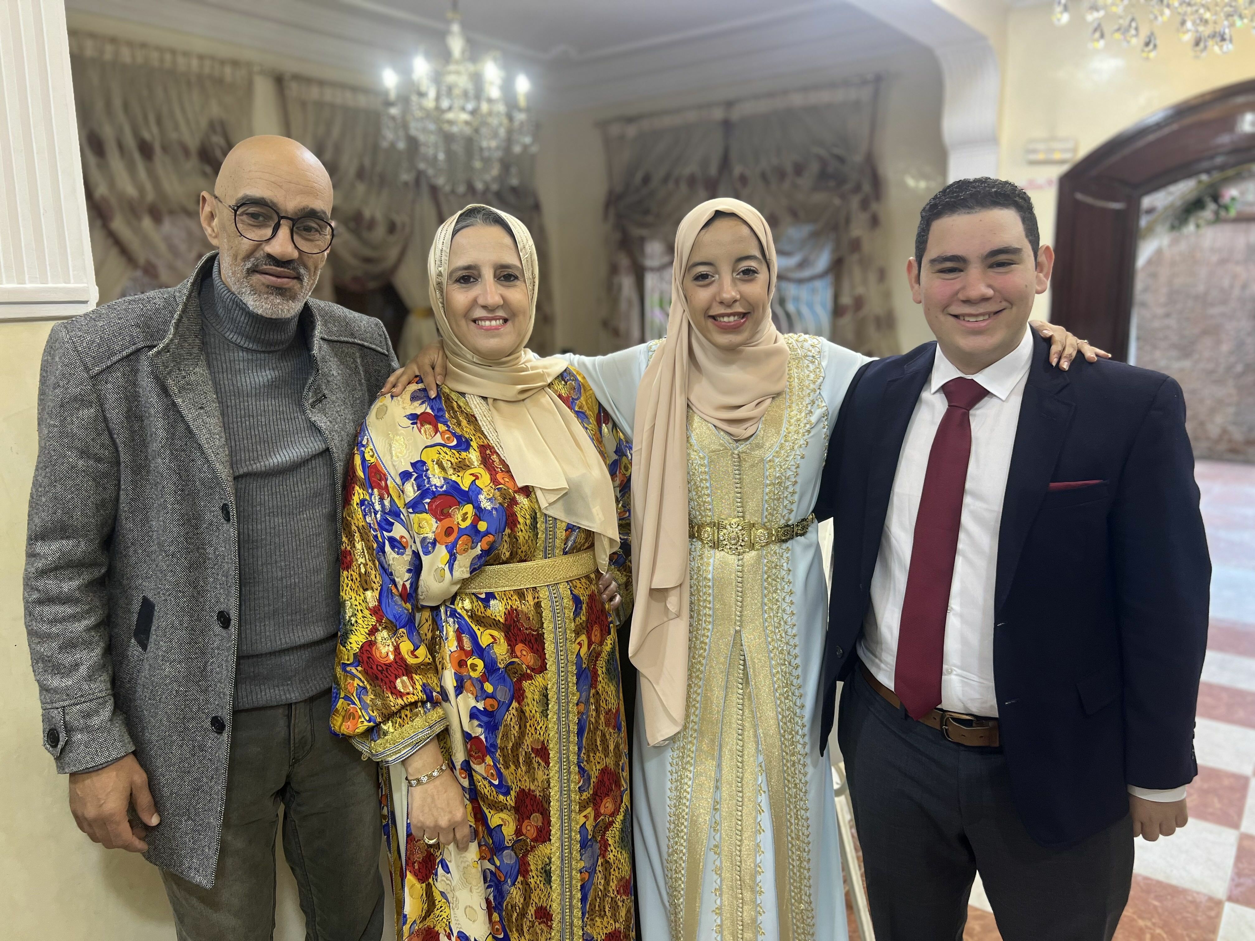 Isaac in a suit smiling in a group photo with host family, who are dressed in festive Moroccan clothing