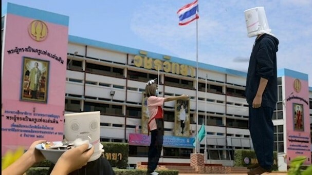 A tall man standing in front of an averaged sized woman in front of the Thai flag
