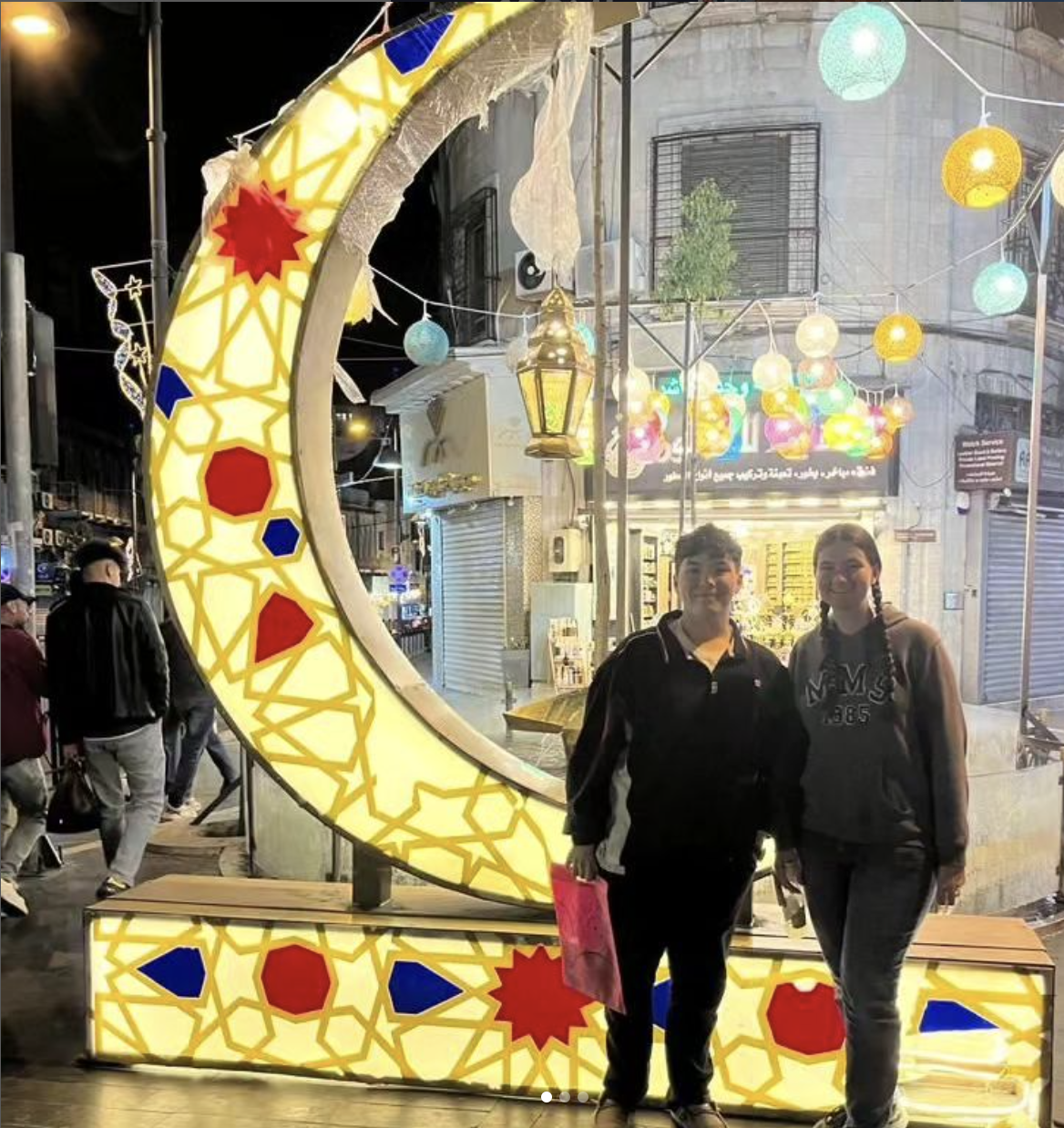 Two people smiling in front of a crescent moon lantern