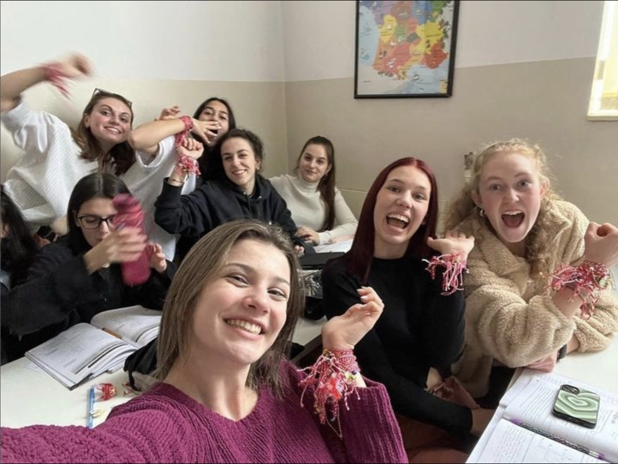Group of students smiling and holding up wrists, which have red and white martenitsa bracelets