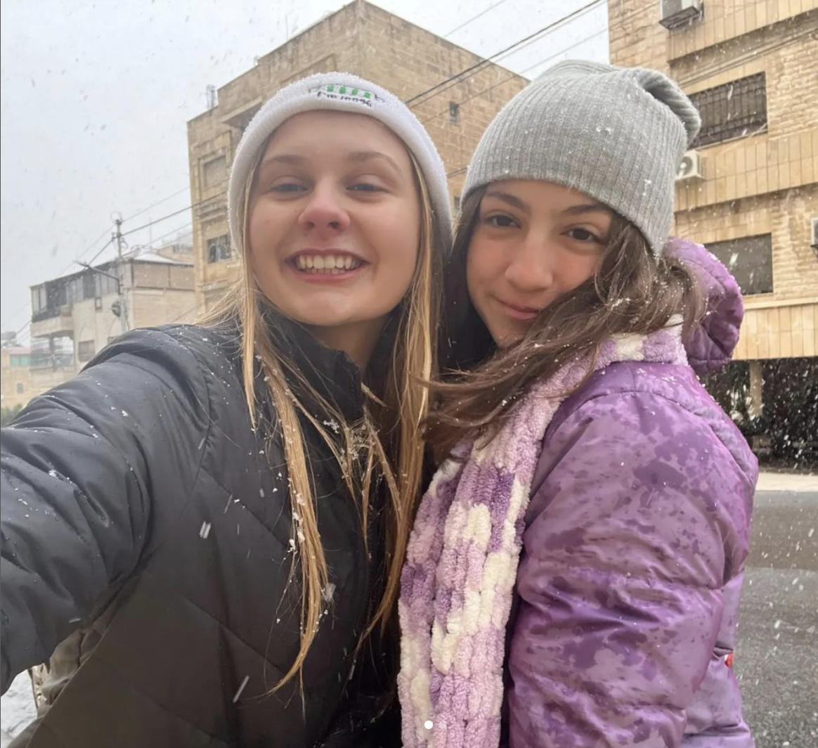 Two girls in hats and coats smiling as snow falls