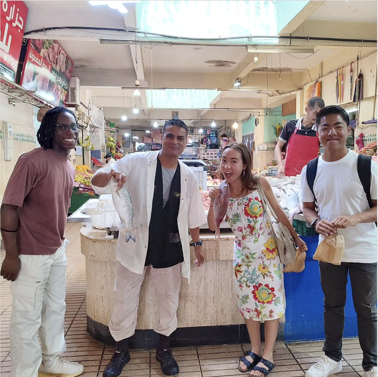 Students pointing to a vendor holding a fish in a Moroccan market