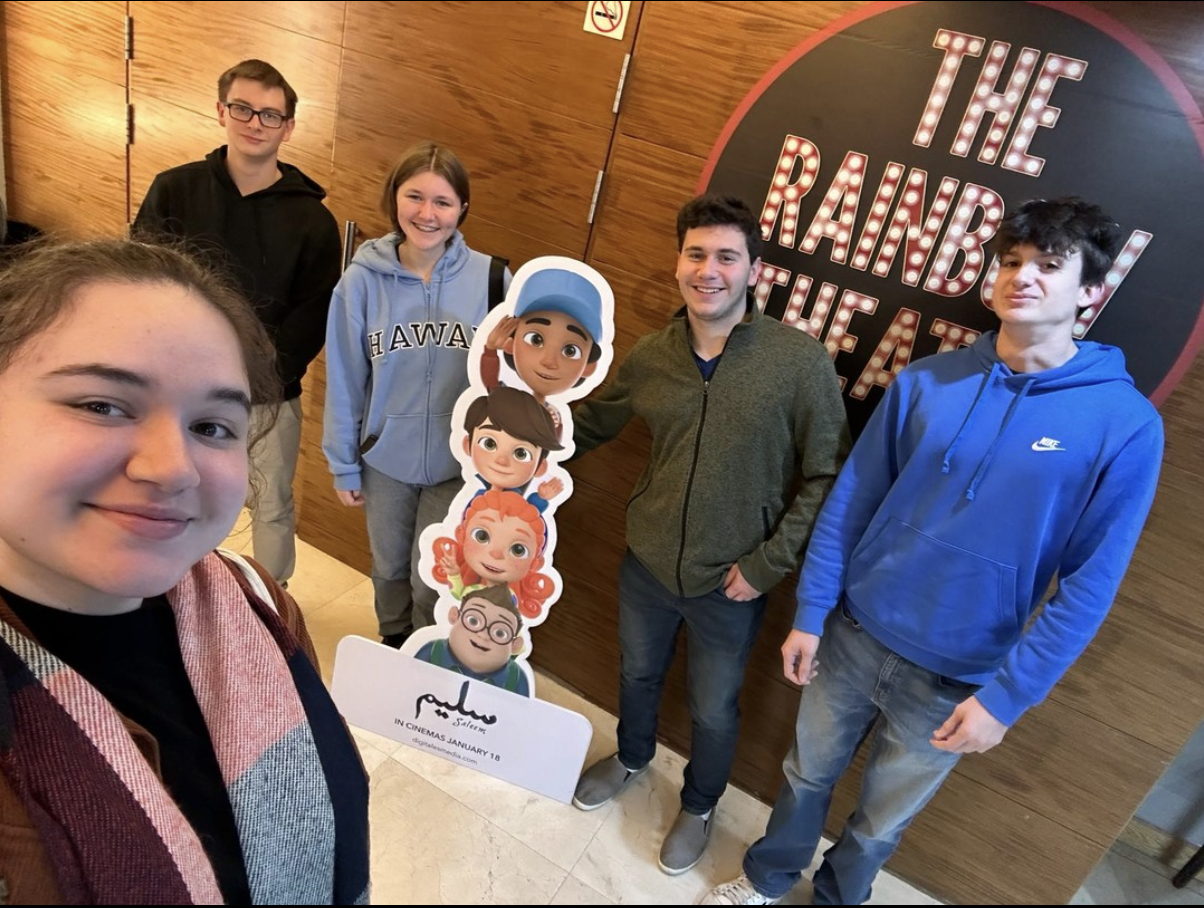 Students smiling in theater hallway in front of a cardboard cutout