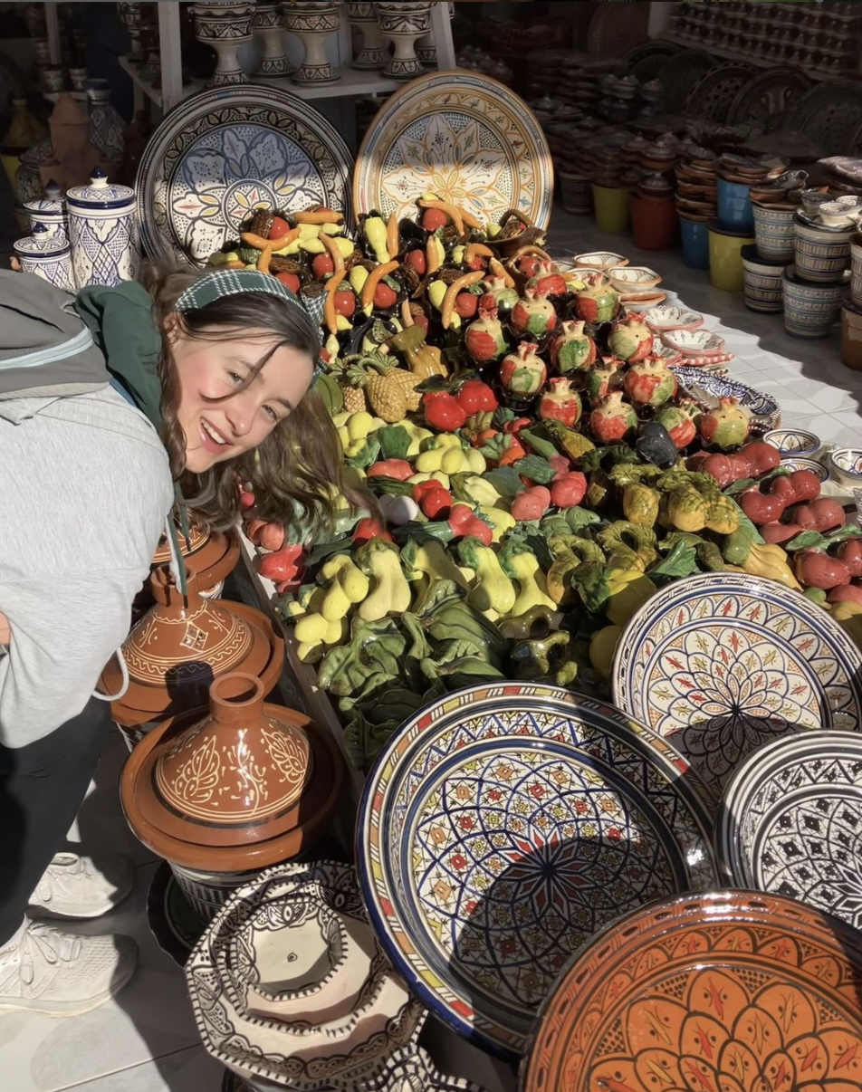 Caroline smiling in front of a table filled with painted, ceramic, Moroccan plates, jars, and tagines
