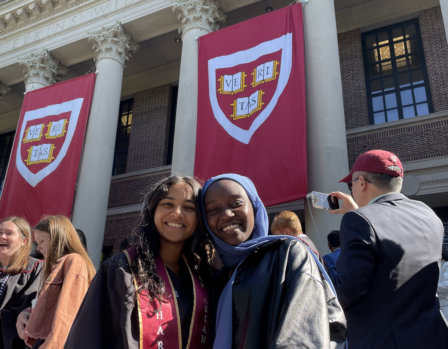 Shruthi in graduation robes with her host sister, smiling in front of a graduation banner