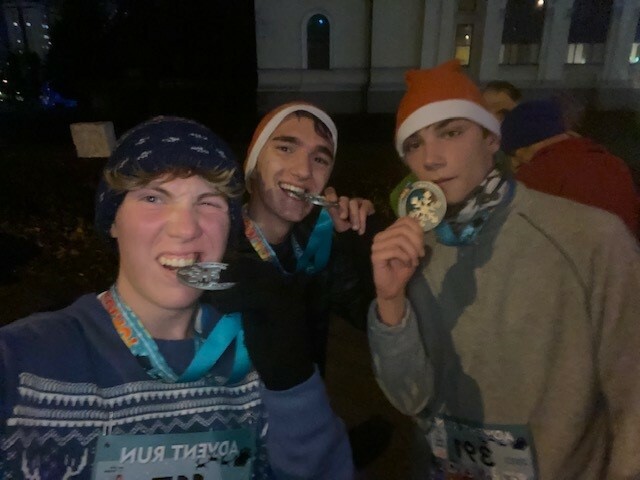 3 students holding their race medals, 2 biting them in celebration