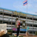 A tall man standing in front of an averaged sized woman in front of the Thai flag