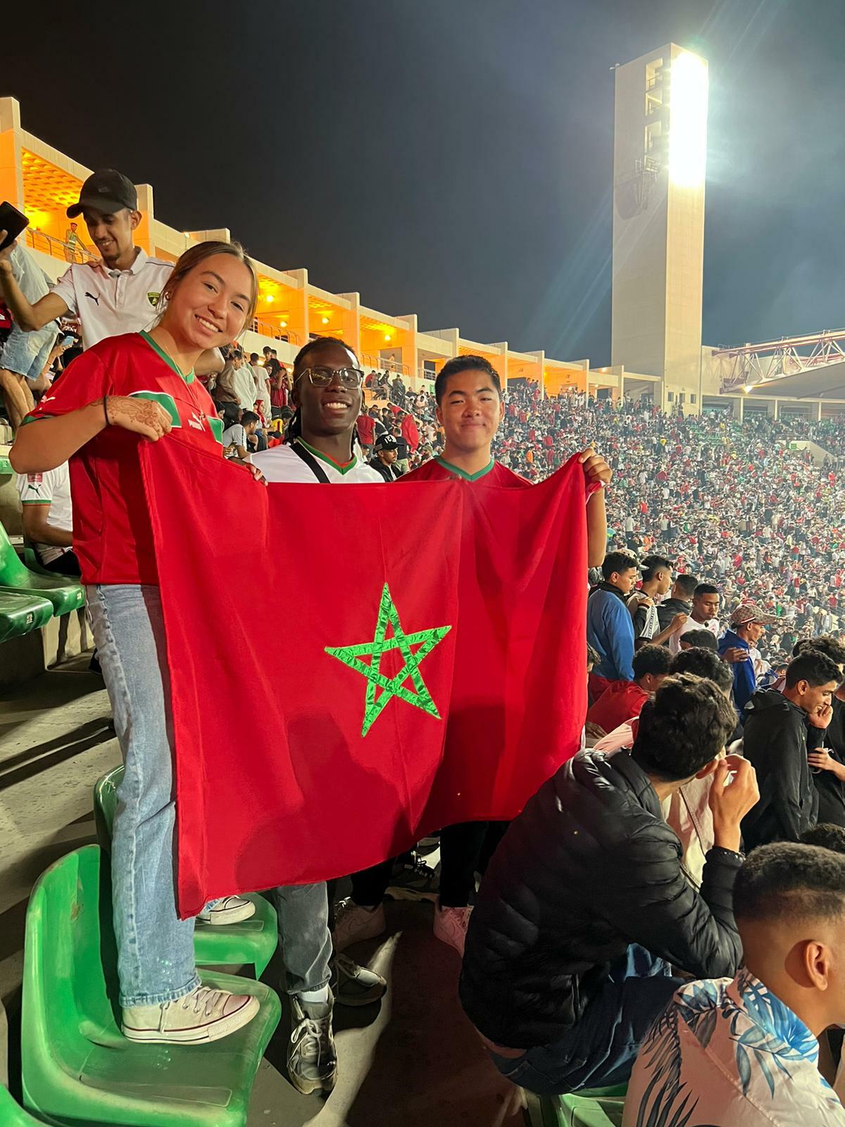 Morocco students in a soccer stadium posing with the Moroccan flag